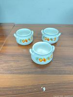 Three ceramic sugar bowls on tabletop showing side fruit motif and handles