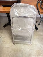Folded beige metal chair wrapped in plastic