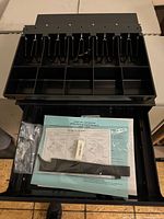 Open cash drawer showing removable tray, paperwork, keys, cable