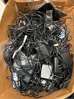 Box filled with tangled assorted AC adapters showing quantity and condition