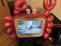 Front view showing red/pink crab plush housing and powered on 19" screen
