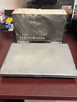 Closed silver HP laptop in front of generic Notebook box