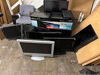 Stacked flat-panel TVs and monitors with Hannspree box and chair for scale