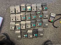 Front view of 24 Plantronics inline adapters arranged in rows with Verifone PIN pad and cables