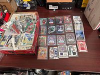 Open storage box filled with several hundred loose football and mixed-sport cards alongside laid-out sleeved autograph, jersey patch and insert cards