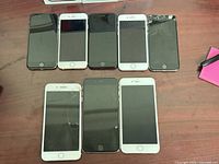Eight iPhones arranged face up showing screens, color variations and visible damage