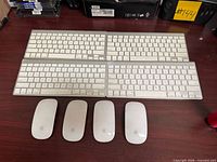 Four Apple wireless keyboards above four Apple Magic Mouse on table