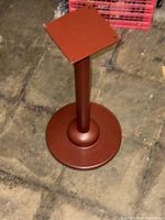 Full view of metal pedestal stand showing round base, cylindrical column, square mounting plate with four holes, matte reddish-brown finish