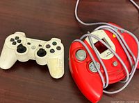 Sony white DualShock 3 controller and red wired Dreamcast controller side by side on table