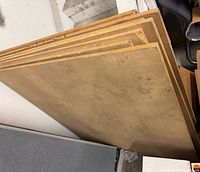 Stack of seven particle board sheets leaning against wall