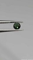 Round green sapphire held in tweezers, side view