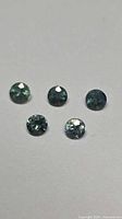 Five round blue-green sapphires on neutral background, showing size and colour.