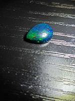 Pear-shape black opal cabochon on dark background showing play-of-color