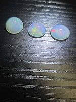 Three Ethiopian opal cabochons on black surface showing play-of-color
