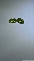 Pair of apple-green oval peridots on neutral background
