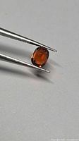 Burnt orange cushion spessartite garnet held by tweezers, angled view