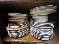 Two stacks of assorted medium and large porcelain plates showing varied colors, patterns and edges