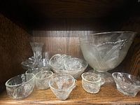 shelf displaying punch bowl, multiple punch cups, teacup, bud vase and cordial glass