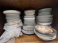 Stacks of assorted small porcelain plates and shallow bowls in cabinet