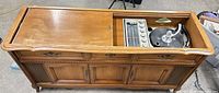 Full front view of Magnavox console showing cabinet, speaker grilles, control drawers, and partially opened sliding top revealing electronics