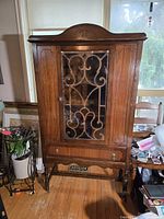 Full view of cabinet front showing glass door, crest, drawer and legs