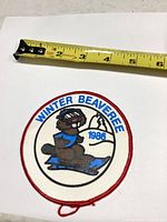 Front of round embroidered patch with measuring tape for scale, showing beaver skiing image and text