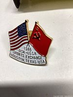 Front view of enamel pin showing crossed flags and text