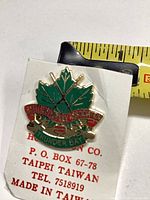 Front of enamel lapel pin on backing card with tape measure showing size