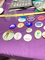 Overview of approx. 13 assorted vintage pinback buttons with measuring tape for scale