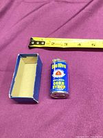 Lighter beside open blue box, measuring tape showing scale