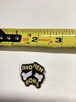 Front view of enamel pin next to tape measure showing size under 1 inch