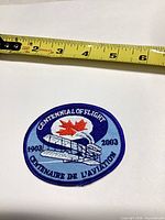 Front view of embroidered aviation commemorative patch next to tape measure for scale