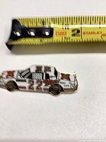front view of enamel race car lapel pin next to tape measure