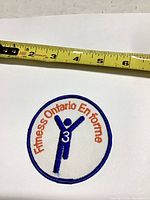 Front view of the round Fitness Ontario patch beside tape measure showing ~3 inch diameter