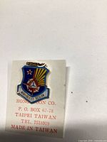 Front view of shield-shaped enamel pin on Hong Boon Co. backing card