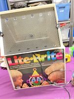 Lite-Brite toy open showing pegboard, branding, cord, pegs and jars visible on table