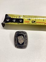 Front view of rectangular Manitoba Wildlife Federation lapel pin beside tape measure