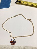 Full view of gold-tone necklace with pendant and tape for scale
