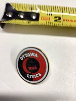 Front of Ottawa Civics enamel pin beside tape for scale