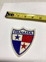 Front of shield patch beside tape measure showing size