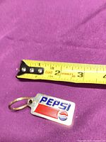 Front of Pepsi keychain beside ruler showing length under 2 inches