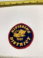 Front view of round Nipissing District 1987 patch next to tape measure