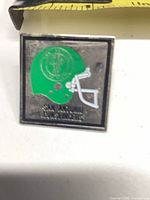 Front view of square enamel pin showing green helmet and team name