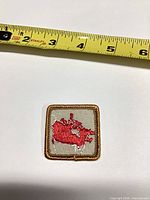 Front view of square Canada map patch beside measuring tape showing size