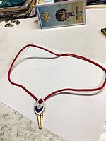 Entire bolo tie laid flat showing red cord and enamel ACT slide