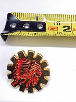 front view showing red Redskins head logo on gold gear shape with tape measure for size reference