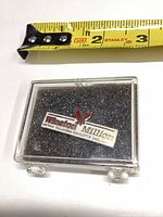 Front view of Winston Million enamel lapel pin in clear display case with ruler showing approximately 1-inch size