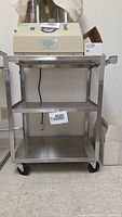 Full view of stainless steel utility cart with three shelves and casters