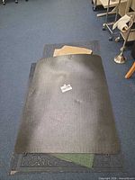 Stack showing black chair mat, dark grey scroll-border rug, green rug edge and beige rugs