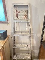 Full view of folded aluminum step ladder showing six steps and paint splatter